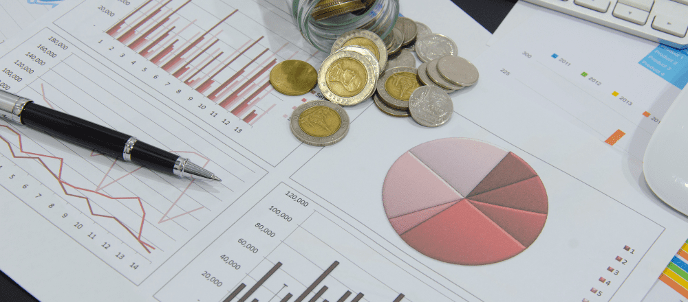 A jar of coins on a desk with a pen and graphs.